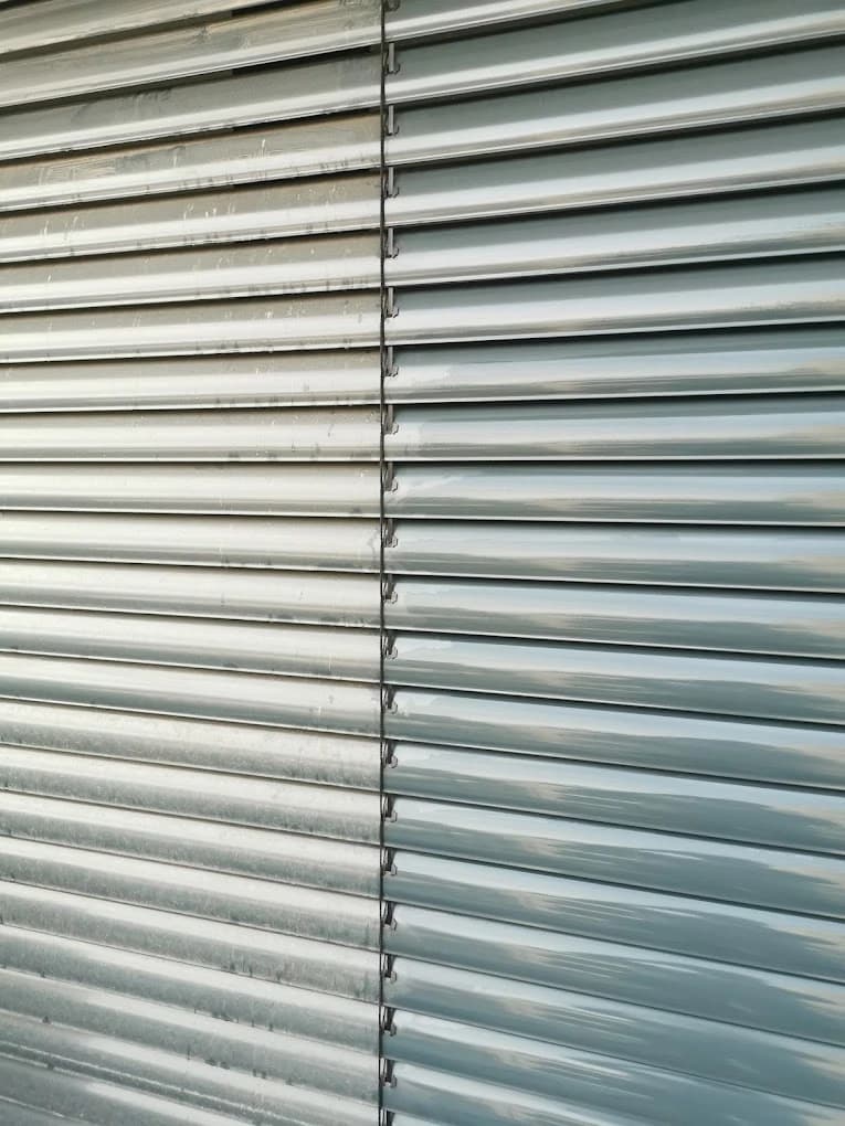 Ein Vorher-Nachher-Vergleich von Jalousien, wobei eine Seite sauber und die andere schmutzig ist. Die saubere Seite zeigt glänzende, reflektierende Oberflächen, während die schmutzige Seite Staub und Flecken aufweist.