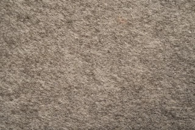 Nahaufnahme einer grauen Filztextur. Die Textur ist rau und ungleichmäßig.