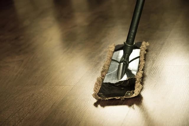 Ein Mopp reinigt einen glänzenden Holzboden. Das Bild zeigt den Moppkopf und einen Teil des Stiels.